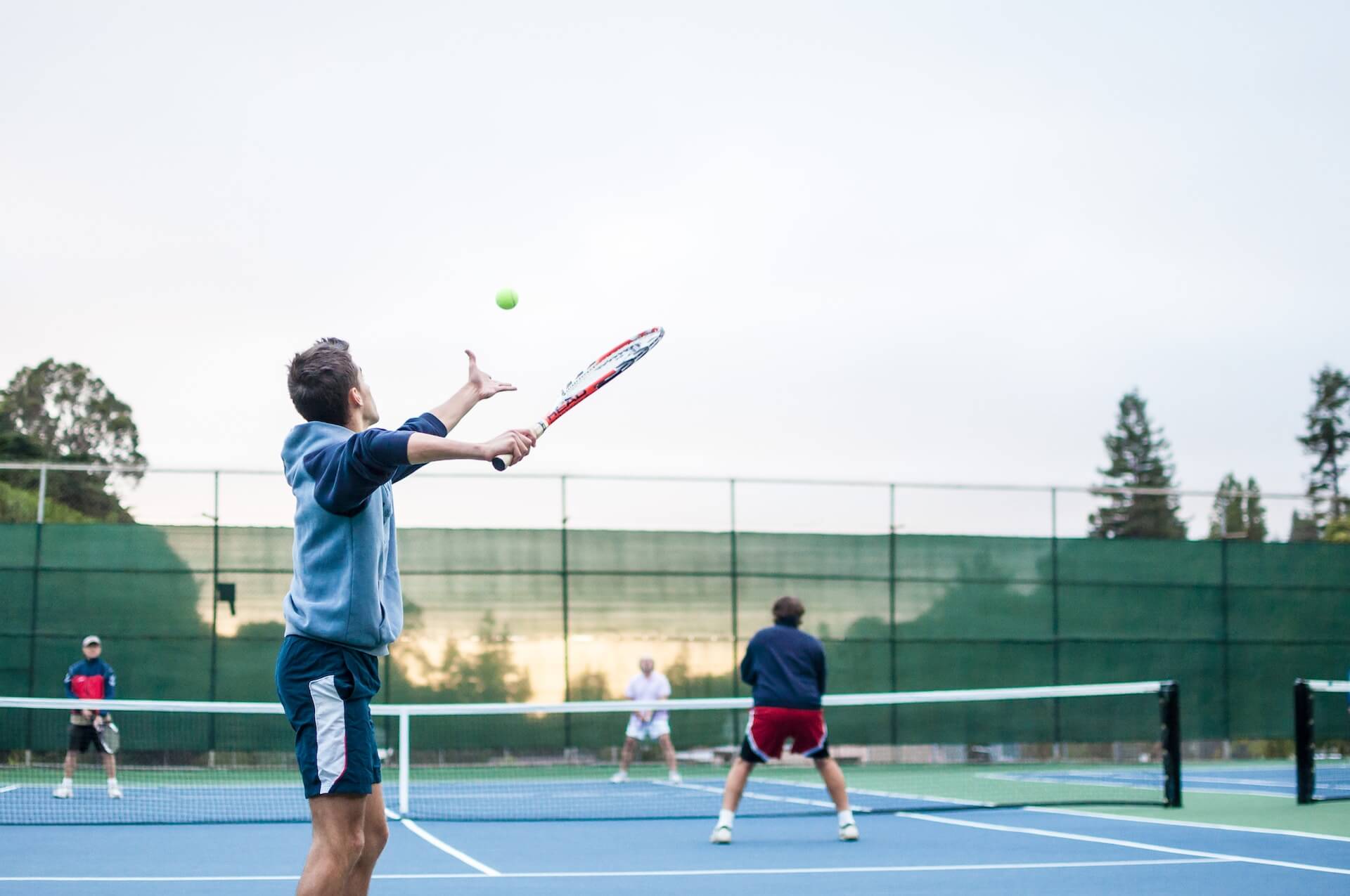 four people playing doubles tennis outdoors